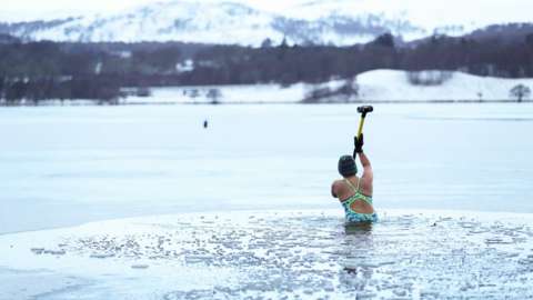 A woman breaks the ice before a swim at Loch Insh in the Scottish Highlands