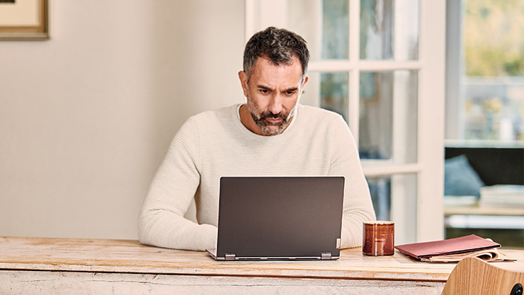 Mees kasutab kodus sülearvutit, istudes pika puulaua taga.