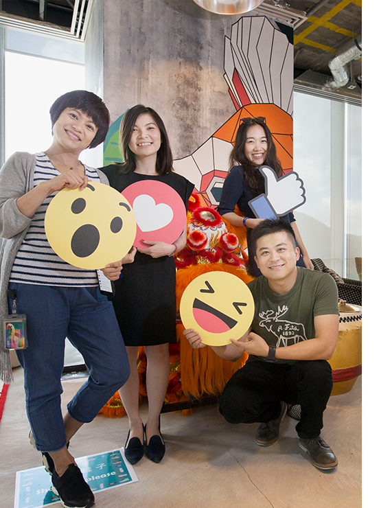 ="People holding cardboard cutouts of four Facebook reactions: 'Wow, 'Love,' 'Like' and 'Haha'"