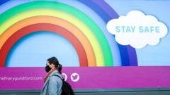 A woman wearing a face mask walks past a rainbow poster with a message to "Stay Safe"